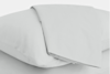 A neatly folded white sheet lies on top of a white pillow, both set against a plain white background.