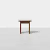 A small, square wooden table with a simple design stands alone on a light gray floor against a plain white background.