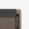 Close-up of the top corner of a wooden bed frame with a light gray upholstered headboard, showing smooth wood grain and minimalist design details against a white background.