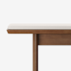 A close-up of a wooden bench with a simple design, featuring a light-colored cushioned seat and clean, straight lines against a plain white background.