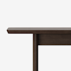 A close-up side view of a dark wooden table against a plain white background, showing the tabletop, edge, and part of one leg.