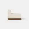 A modern armless sofa chair with light beige upholstery and a wooden base, shown from the back and side, on a plain light background.