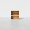A wooden shelving unit with three compartments, including two shelves and a larger open space at the bottom, standing on a light gray floor against a plain white background.