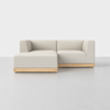 A modern, light beige L-shaped sectional sofa with wooden base sits on a smooth, light-gray floor against a plain white background.