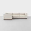 A modern, L-shaped sectional sofa with light beige upholstery and a wooden base, set against a plain white background on a light gray floor.