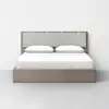 A modern, minimalist bed with a light wooden frame, a padded gray upholstered headboard, and white bedding with two pillows, set against a plain white wall and floor.