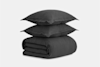 Two dark gray pillows are stacked neatly on top of a matching folded comforter, all set against a plain white background.