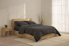 Two dark gray pillows are stacked neatly on top of a matching folded comforter, all set against a plain white background.