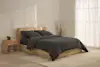 Two dark gray pillows are stacked neatly on top of a matching folded comforter, all set against a plain white background.