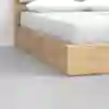 Close-up view of a modern wooden bed frame with white bedding and pillows, positioned on a smooth light gray floor next to a white wall.