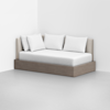 A modern daybed with a light wood frame, beige upholstered backrest, white mattress, and four white pillows, placed in a minimal corner of a white room with a light gray floor.