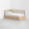 A minimalist daybed with a light wood frame and beige upholstered backrest sits in the corner of a white room, featuring a neatly made bed with white sheets and a single pillow.