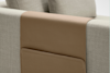A close-up of a light gray fabric sofa with a tan leather organizer draped over the backrest, featuring a stitched pocket for holding items.