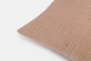 Close-up of the corner of a light brown, textured fabric pillow on a white background. The pillow’s fabric has a crinkled, striped pattern.