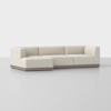 A modern L-shaped sectional sofa with off-white upholstery and a low wooden base, displayed in a minimalist, light gray studio setting.