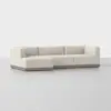 A modern L-shaped sectional sofa with off-white upholstery and a low wooden base, displayed in a minimalist, light gray studio setting.