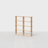 A minimalist, light wood bookshelf with four shelves and three vertical dividers, standing empty against a plain, light gray background.
