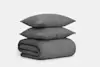 Two dark gray textured pillows are stacked on top of a neatly folded matching blanket against a plain white background.
