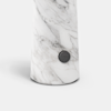 A cylindrical white marble object with grey veins stands upright; a small round black button or knob is attached near its base. The background is plain white.
