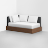 A modern daybed with a dark upholstered backrest, white bedding, and four white pillows, featuring a wooden frame base, is placed in the corner of a minimalist room with white walls and a light gray floor.