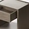 A minimalist, light wood cabinet stands on a plain white background. The cabinet has a single drawer, which is partially open, revealing the inside. The design is modern and simple.