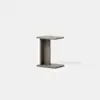 A modern, minimalist side table with an I-shaped design in light brown wood, placed on a smooth, light gray surface against a plain white background.