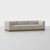 A modern beige three-seat sofa with square arms and a low wooden base, placed on a light gray floor against a plain white background.