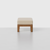 A minimalist ottoman with a light beige cushioned top and a simple wooden base, photographed against a plain white background. The design is modern and clean.