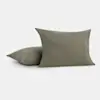 Two olive green square pillows, one upright and the other lying flat, on a plain white background. The pillows have a smooth, linen-like texture.