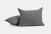 Two textured gray pillows are shown against a plain white background, with one pillow standing upright and the other lying flat, partially overlapping each other.