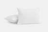 Two white, rectangular pillows with a subtle checkered texture are placed against a plain white background; one pillow is upright, while the other lies flat behind it.
