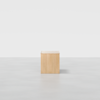 A simple, light wooden cube sits alone on a smooth, light gray floor against a plain white background.