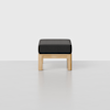 A minimalist bench with a light wooden frame and a rectangular, dark gray cushioned seat, set against a plain white background.