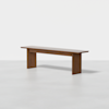 A minimalist wooden bench with a flat rectangular seat and two wide, sturdy legs, set against a plain white background.
