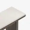A close-up of the corner of a rectangular bench with a light beige upholstered cushion and a dark wooden frame, set against a white background.