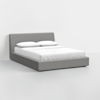 A modern grey upholstered bed with a low profile and angled headboard, dressed in white sheets and two white pillows, set against a plain white background.