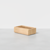 A rectangular wooden storage box with open sides, placed on a light grey surface against a plain white background.