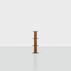 A minimalist, vertical wooden shelf with four tiers stands alone in a bright, empty room with white walls and a light floor.