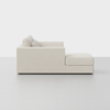 Side view of a modern, light beige sectional sofa with a chaise lounge on a light gray floor and a plain white background. The sofa has clean lines and plush cushions.