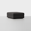 A square, dark gray upholstered ottoman with a minimalist design sits on a light, seamless floor against a plain white background.