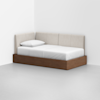 A modern daybed with a wooden base, white bedding, and light beige upholstered back and side panels, placed in the corner of a minimalist white room.