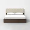 A modern bed with a dark wooden frame, upholstered beige headboard, white sheets, and two white pillows, set against a plain white wall on a light gray floor.
