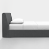 A modern, minimalist bed with a grey upholstered frame and headboard, neatly made with white sheets, a white blanket, and a white pillow, set against a plain white background.