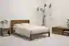 Minimalist bedroom with a wooden bed frame, beige bedding, a matching nightstand and dresser, potted plants, a framed wall art piece, and neutral-colored carpet. The room has a calm, modern atmosphere.