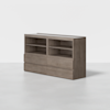 A modern, light wood cabinet with four open shelves on top and four drawers below, standing on a seamless light gray floor against a plain white background.