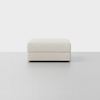 A square, light beige upholstered ottoman with a minimalist design sits on a smooth, light gray floor against a plain white background.