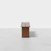 A minimalist wooden bench with clean lines, viewed from the end against a plain white background. The bench has a rectangular seat and solid sides, casting a subtle shadow on the floor.