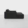 Side view of a modern, dark gray sectional sofa with a chaise lounge on the right, placed in a minimal, light-colored room with a plain background.
