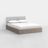 A modern bed with a light grey upholstered headboard, white bedding, and a light wood platform base, set against a plain white wall and floor.