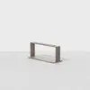 A minimalist wooden bench with a rectangular open frame design, positioned on a light gray, slightly reflective floor against a plain white background.
